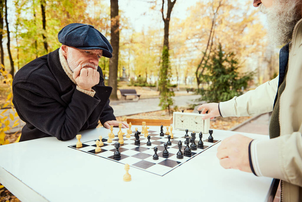 Portrait of senior man playing chess in the park on a daytime in fall. Concept of leisure activity, friendship, sport, autumn season, game, entertainment, old generation, retirement - Фото, изображение