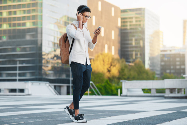 Telefon, zene és a város egy férfi diák sétál egyetemre vagy főiskolára a reggeli ingázás közben. Fejhallgató, közösségi média és 5 g-os mobiltechnológia egy városi városban élő férfi tanulóval sétálni. - Fotó, kép