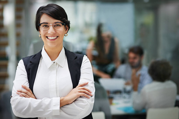 La fiducia porta al successo. Ritratto di una giovane donna d'affari in piedi in un ufficio con colleghi sullo sfondo - Foto, immagini