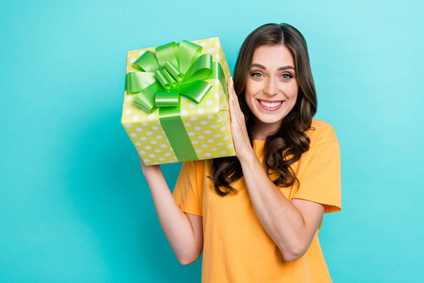 Portrait photo of young cute nice girl wear orange t-shirt toothy smile hold big gift surprise enjoy anniversary surprise isolated on cyan color background. - Foto, Imagem
