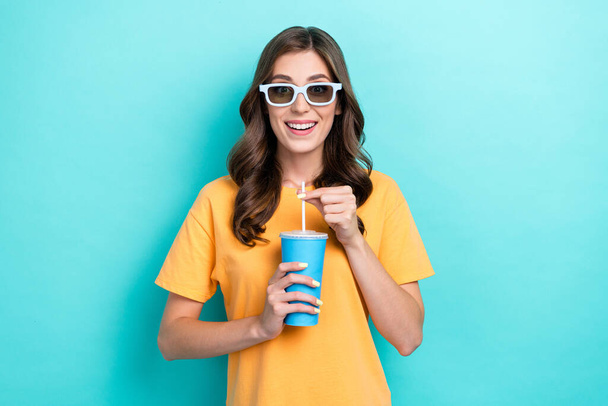 Photo of young adorable cute pretty nice woman wear yellow t-shirt hold cup cola soda wear glasses watching film tv isolated on cyan color background. - Фото, изображение
