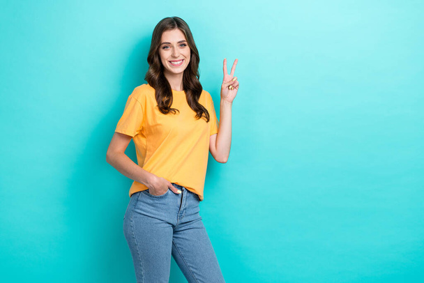 Photo of pretty cute lady wear yellow t-shirt smiling showing v-sing empty space isolated turquoise color background. - Foto, imagen