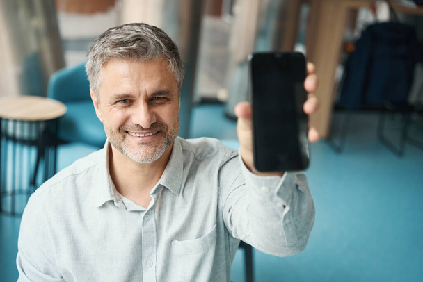 Довольный человек держит телефон в руке, он показывает экран собеседнику - Фото, изображение