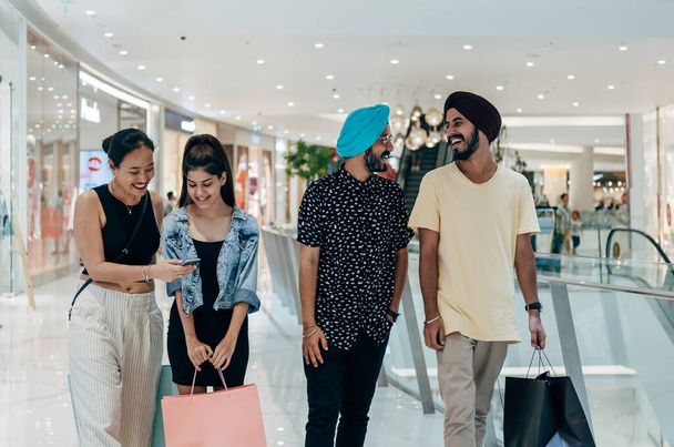 Mutlu çoklu etnik arkadaşlar alışveriş torbaları taşıyor ve alışveriş merkezinde birlikte eğleniyorlar. - Fotoğraf, Görsel