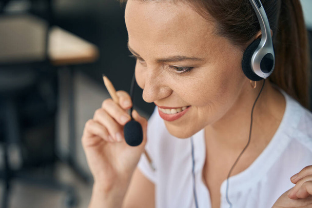 Top view close up of woman using headphones with microphone while sitting in office during working day - Zdjęcie, obraz