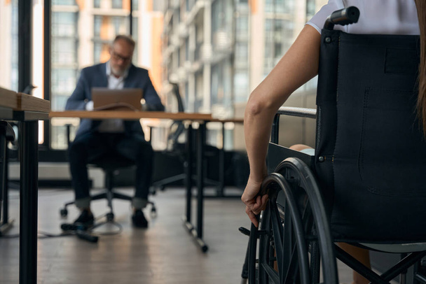 lähikuva naisesta, joka käyttää pyörätuolia, kun hän menee haastattelemaan miespuolista kollegiota, joka istuu pöydän ääressä muistikirjan kanssa - Valokuva, kuva