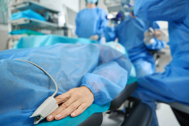 Pacjent w niebieskim kombinezonie ochronnym leżący na kanapie w sali operacyjnej w szpitalu - Zdjęcie, obraz