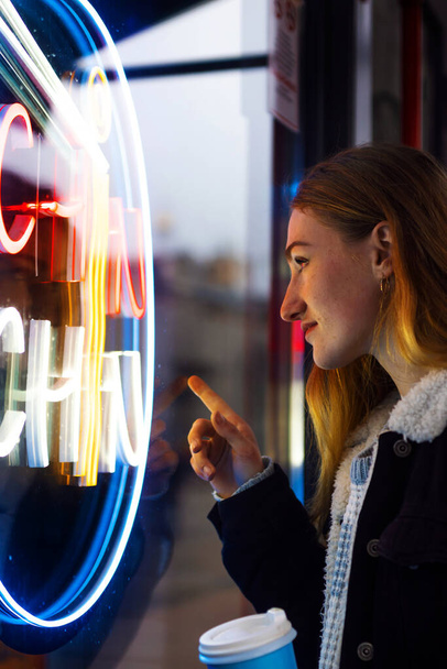 młoda kobieta turysta z lekkim makijażem rozgląda się w pobliżu baru z kolorowym neonem przed megalopolis nocy. - Zdjęcie, obraz