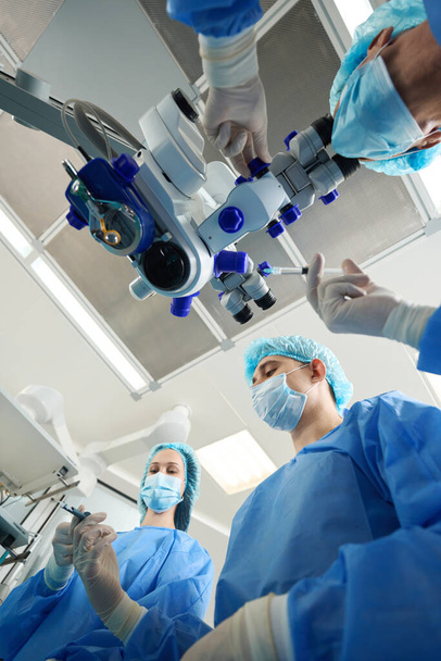 Nahaufnahme von Ärzten in Schutzanzügen und Masken, die ein medizinisches Instrument in der Hand halten und eine Operation durchführen - Foto, Bild