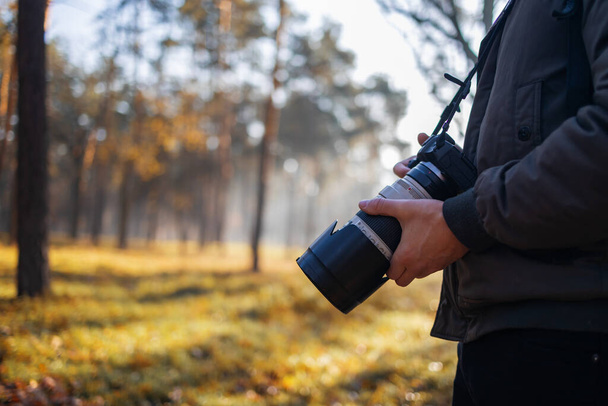 Νεαρός φωτογράφος φωτογραφίζει στο δάσος. φωτογράφος με μεγάλη επαγγελματική κάμερα. - Φωτογραφία, εικόνα