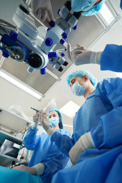 Close-up foto van medisch personeel in beschermende pakken en maskers met medisch instrument en uitvoeren van een operatie - Foto, afbeelding