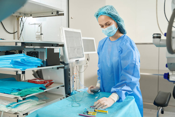 Verpleegster in de buurt van het scherm van medische apparatuur en vasthouden aan de tafel met instrumenten - Foto, afbeelding