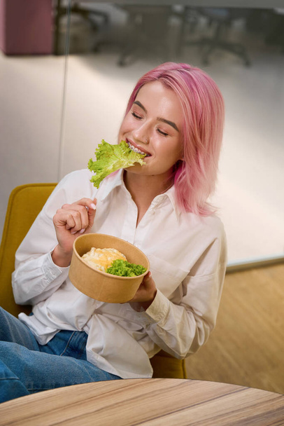 Jongedame met roze haar aan tafel, met eco bord met gezond veganistisch eten en eten - Foto, afbeelding