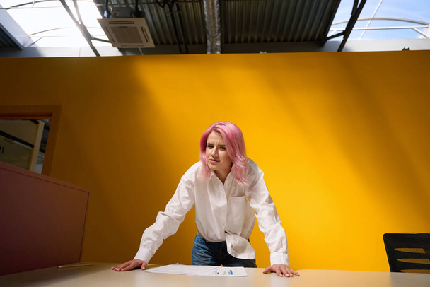 Lady with pink hair standing office near table with yellow bright background and looking at camera - Fotoğraf, Görsel