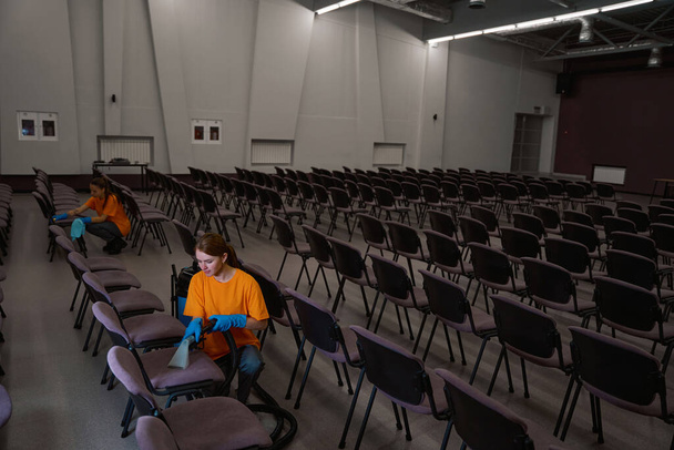 Два профессиональных очистителя пылесосят и дезинфицируют обивку в зале для презентаций - Фото, изображение