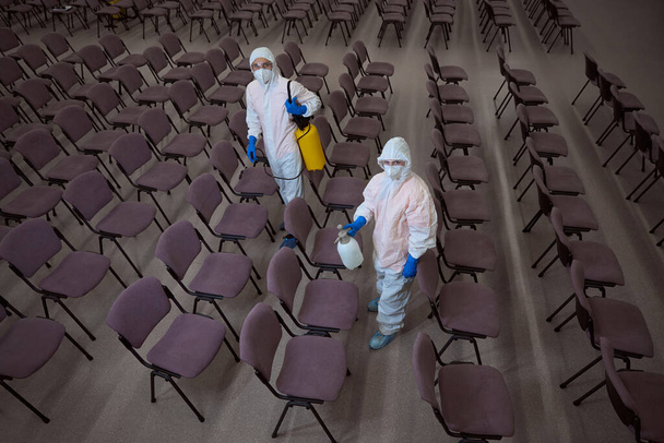 İki profesyonel temizlikçi koruyucu giysiler içinde ellerinde kimyasal malzemelerle kameraya bakıyor. - Fotoğraf, Görsel