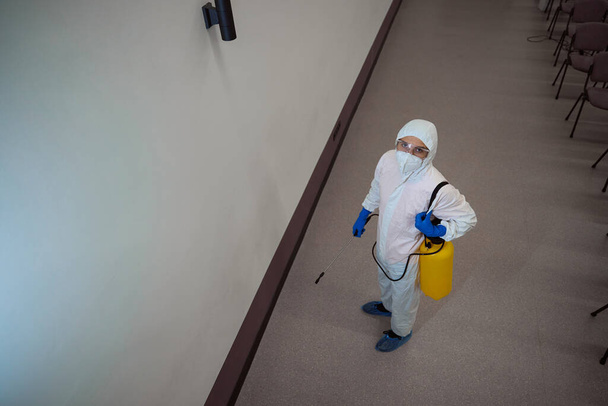 Entschlossener Reinigungsdienstmitarbeiter in Schutzausrüstung blickt in die Kamera, während er sich auf die Sanierung des Gebäudes vorbereitet - Foto, Bild
