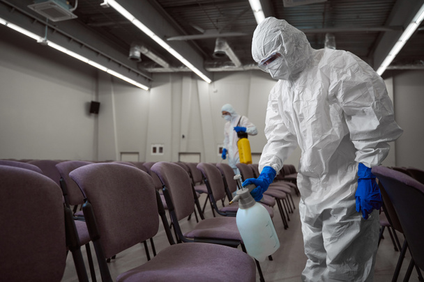 Professionelle Reinigungskräfte halten sich an Sicherheitsprotokolle und tragen Schutzanzüge, während sie Möbel mit Chemikalien desinfizieren - Foto, Bild