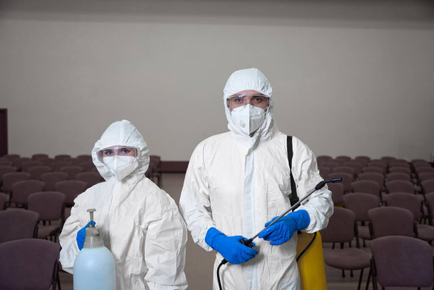 Foto de cintura para arriba de dos limpiadores en trajes de protección general y gafas posando con equipo de limpieza - Foto, imagen