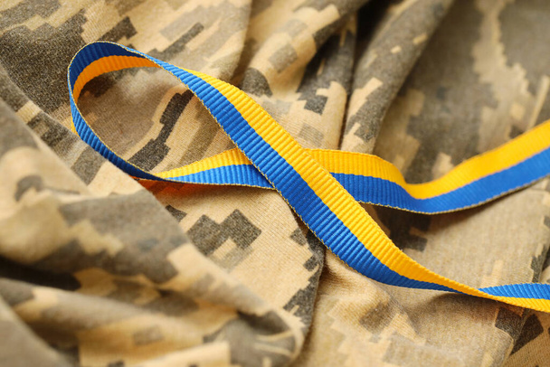 Pixeled digital military camouflage fabric with ribbon in blue and yellow colors. Attributes of ukrainian patriotic soldier uniform - Фото, зображення