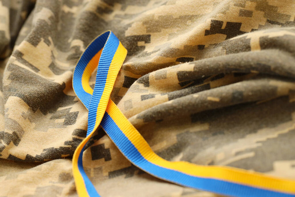 Pixeled digital military camouflage ύφασμα με κορδέλα σε μπλε και κίτρινο χρώμα. Χαρακτηριστικά της ουκρανικής πατριωτικής στρατιωτικής στολής - Φωτογραφία, εικόνα