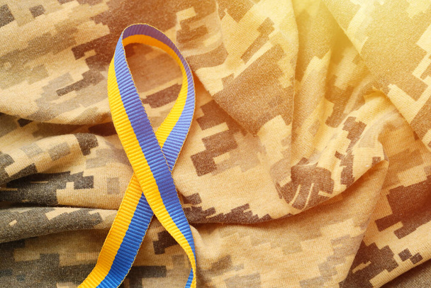 Pixeled digital military camouflage fabric with ribbon in blue and yellow colors. Attributes of ukrainian patriotic soldier uniform - Photo, Image