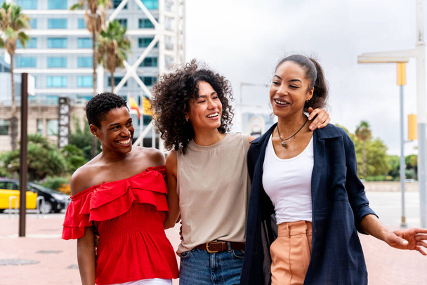 Happy beautiful hispanic south american and black women meeting outdoors and having fun - Black adult females friends spending time together and walking in the city for shopping - Foto, imagen