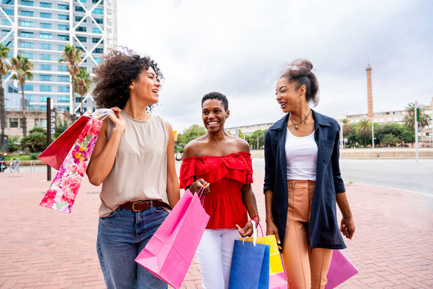 Happy beautiful hispanic south american and black women meeting outdoors and having fun - Black adult females friends spending time together and walking in the city for shopping - Valokuva, kuva