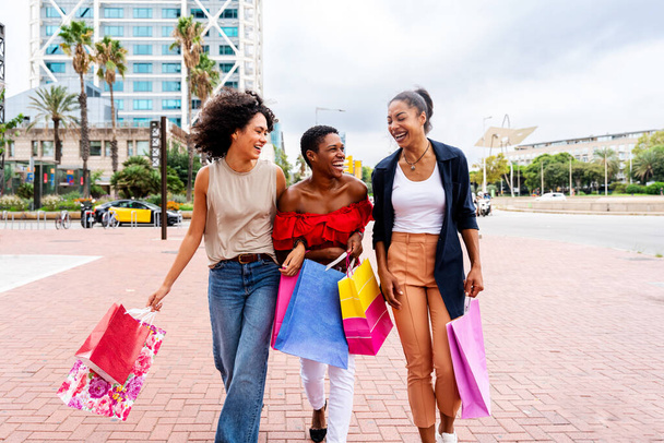 Happy beautiful hispanic south american and black women meeting outdoors and having fun - Black adult females friends spending time together and walking in the city for shopping - Foto, Bild