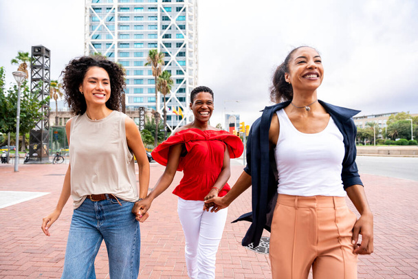 Happy beautiful hispanic south american and black women meeting outdoors and having fun - Black adult females friends spending time together and walking in the city for shopping - Фото, изображение