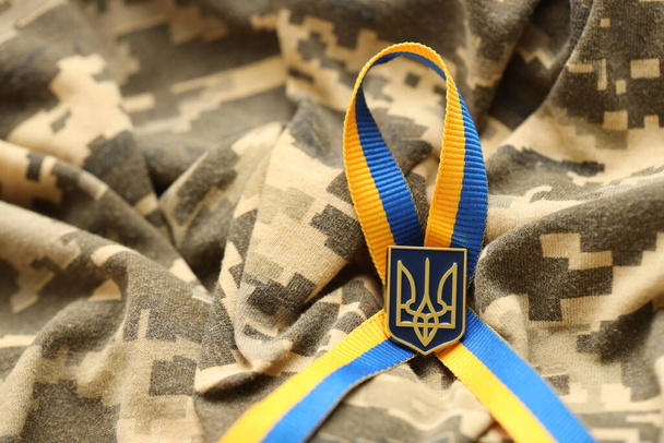 Tissu de camouflage militaire numérique pixellisé avec drapeau ukrainien et armoiries sur ruban rayures aux couleurs bleu et jaune. Attributs de l'uniforme de soldat ukrainien - Photo, image