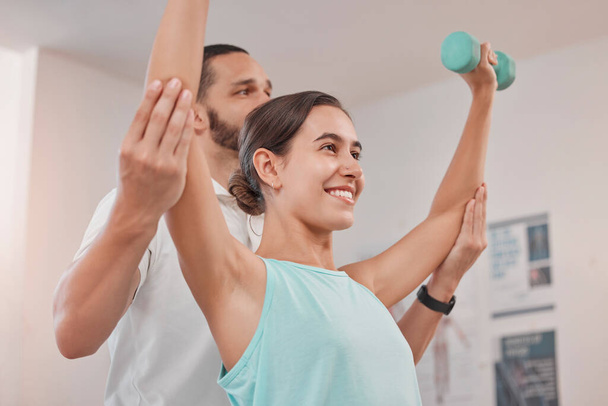 Physical therapy, dumbbell and woman exercise during recovery with physical therapist, happy and hope at clinic. Physiotherapy, support and help from physiotherapist in consultation room for patient. - Φωτογραφία, εικόνα
