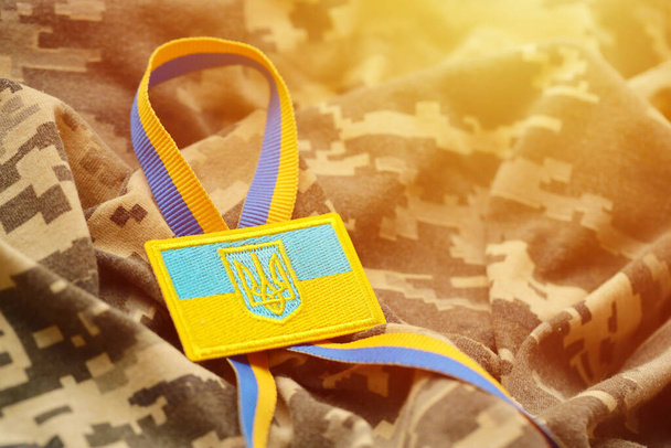 Tela de camuflaje militar digital pixelada con bandera ucraniana y escudo de armas en chevron en colores azul y amarillo. Atributos del uniforme de soldado ucraniano - Foto, imagen