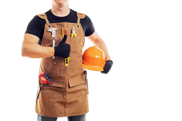 Ανάδοχος εργάτης ή ξυλουργός σε ποδιά εργαζομένων με εργαλεία και κράνος κρατώντας τους αντίχειρες επάνω απομονώνονται σε λευκό φόντο. - Φωτογραφία, εικόνα