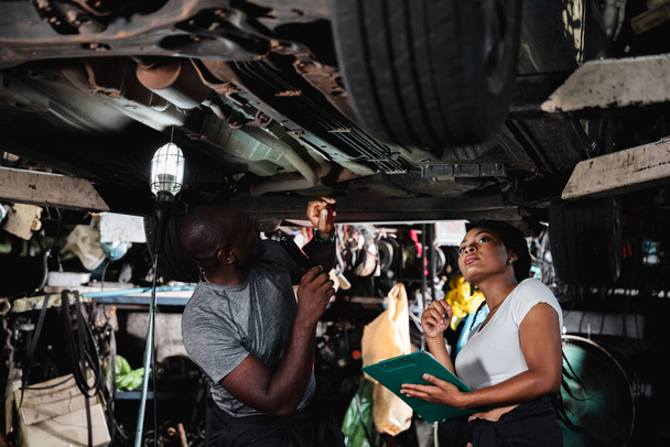 Due meccanici ispeziona e checklist le parti sotto l'auto in garage - Foto, immagini