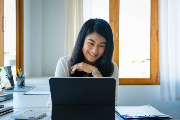 A female entrepreneur or businesswoman shows a smiling face while using a tablet computer for video conferance working on a wooden table - Zdjęcie, obraz