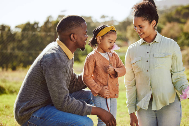 Happy family, nature and child smell flowers while relax in countryside Spring field with mother, father or parents. Love, freedom peace or harmony for black man, woman and kid girl with floral plant. - 写真・画像