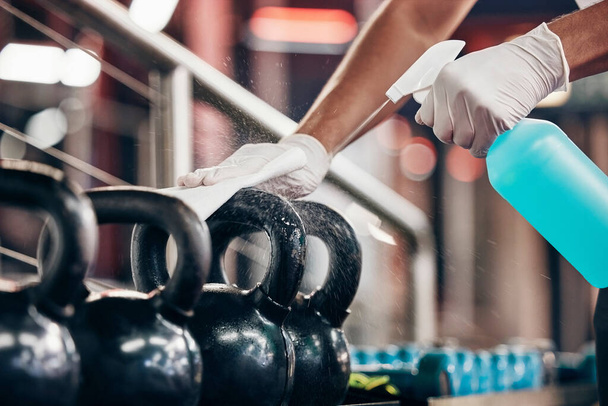 Kettlebell, cleaning service and hands cleaning at a gym with liquid soap in spray bottle with cloth in gloves. Janitor or cleaner wipes dirty bacteria on dusty weights or fitness training equipment. - Foto, imagen