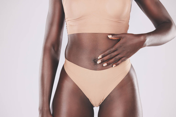 Ręka, brzuch i ciało z modelką czarną kobietą dotykającą swojego brzucha w studio na szarym tle dla odnowy biologicznej. Zdrowie, bielizna i dieta z kobietą pozującą do zdrowego odżywiania lub stylu życia. - Zdjęcie, obraz