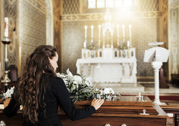 Begrafeniskist, dood en vrouw in de kerk na het verlies van familie, vriend of geliefde van kanker. Scheuren, rouwen en achteraanzicht van vrouw met bloemen op houten kist in kathedraal voor begrafenisceremonie. - Foto, afbeelding