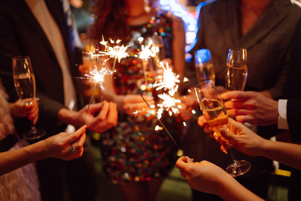 Sparkling sparklers in the hands of friends. Young people having fun with fire sparklers at night time. Holidays, vacation, relax, party and lifestyle concept. - 写真・画像