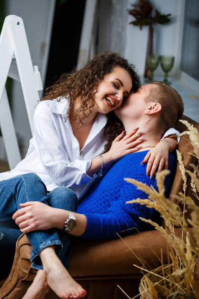 Une fille en chemise blanche et un mec dans un tourbillon bleu sont assis sur un fauteuil et embrasser, embrasser, tendresse, amour - Photo, image