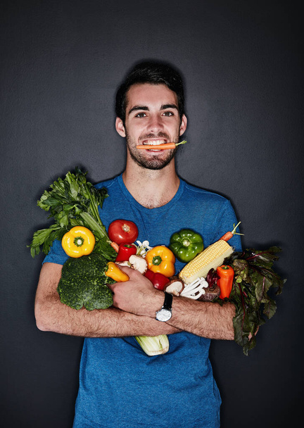 Dokonałem zdrowego wyboru. Studio portret młodego człowieka niosącego na ciemnym tle garść zdrowych warzyw - Zdjęcie, obraz
