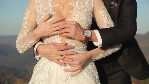 Жених обнимает невесту в белом платье и надевает обручальное кольцо на палец - Кадры, видео
