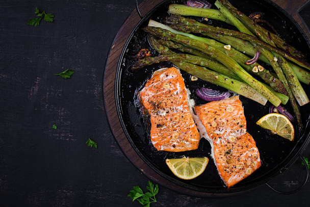 Delicious baked salmon with asparagus, lemon slices and spices on dark table. Top view, flat lay - Photo, Image