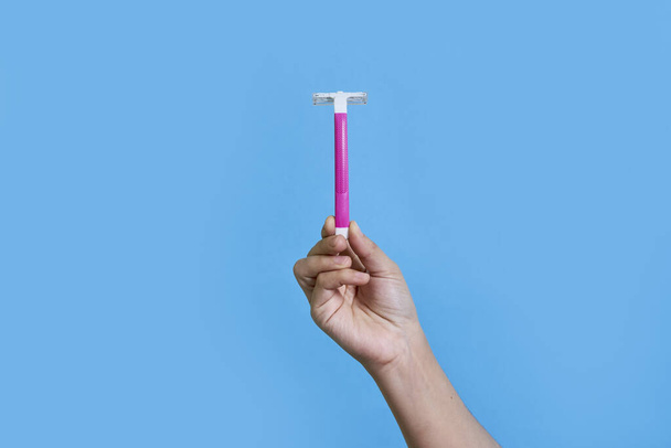 someones hand holding a pink toothbrush against a blue background with copy space in the top right corner - Photo, Image