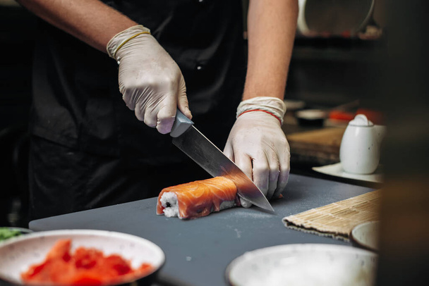 Chef-kok sneed verse sushi broodjes met scherp mes op de snijplank in restaurant. handen dicht - Foto, afbeelding