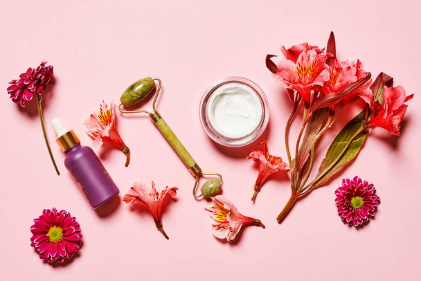 fiori e cosmetici su sfondo rosa con la parola amore scritta in lettere bianche, circondata da vari tipi di prodotti per la cura della pelle - Foto, immagini