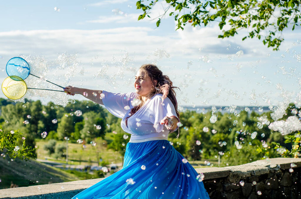 Artista callejera, hermosa mujer joven en falda azul y blusa blanca, con burbujas de jabón muestra programa de jabón en verano en el parque al aire libre para niños - Foto, Imagen