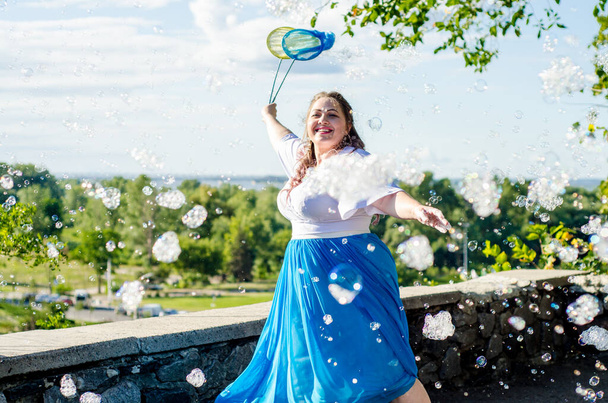 Street performer, beautiful young woman in blue skirt and white blouse, with soap bubbles shows soap show in summer in open air park for children - Foto, Imagem